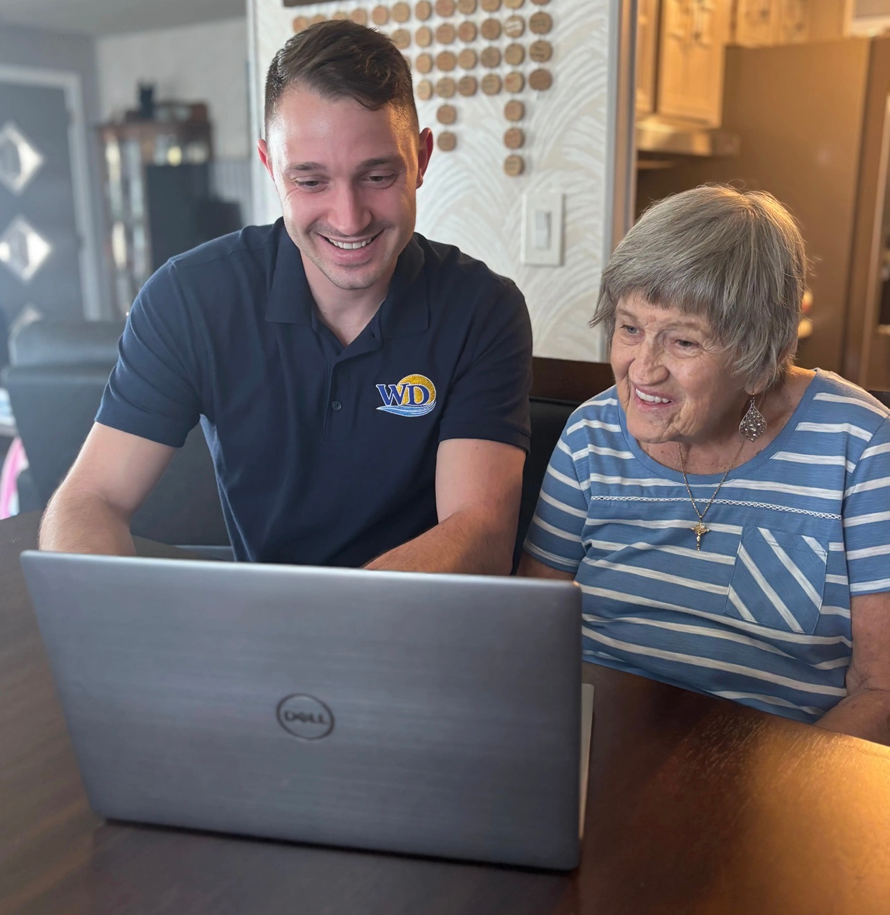 Kyle helping a customer with their tablet and computer at the kitchen table.